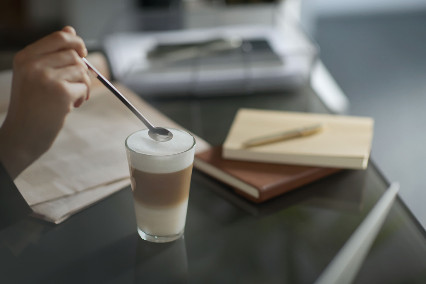 Coffee being prepared beside workplace notebooks